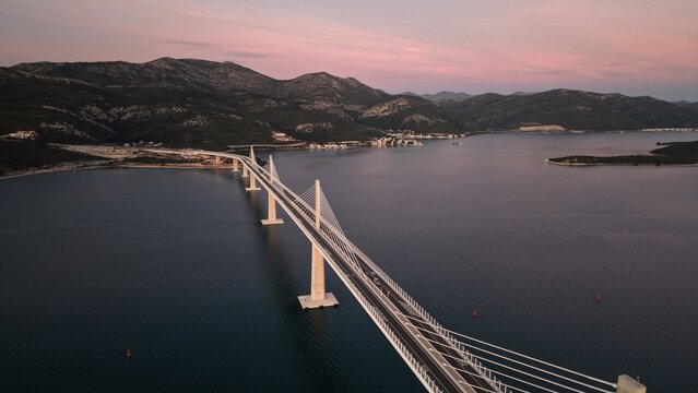 High-angle perspective of Peljesac Bridge over the Adriatic Sea during twilight. Professional drone photography of Croatia's landmark infrastructure at golden hour.