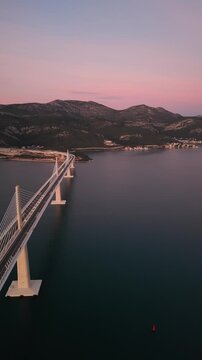 High-angle perspective of Peljesac Bridge over the Adriatic Sea during twilight. Professional drone photography of Croatia's landmark infrastructure at golden hour.