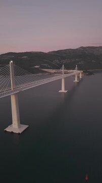 High-angle perspective of Peljesac Bridge over the Adriatic Sea during twilight. Professional drone photography of Croatia's landmark infrastructure at golden hour.