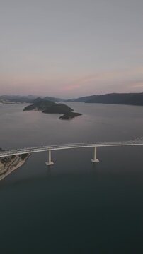 High-angle perspective of Peljesac Bridge over the Adriatic Sea during twilight. Professional drone photography of Croatia's landmark infrastructure at golden hour.