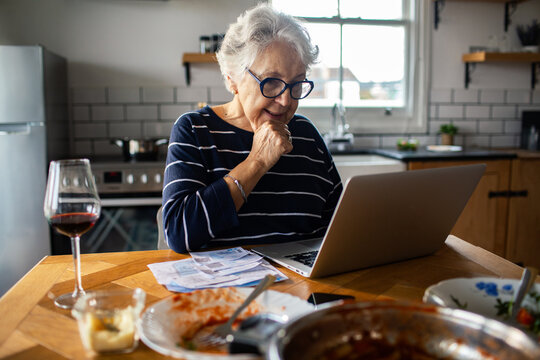 Senior woman paying bills online at kitchen table