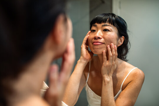 Smiling woman checking skin in bathroom mirror