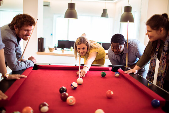 Diverse coworkers playing billiards in modern office