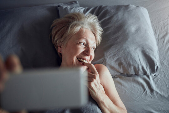 Smiling senior woman taking selfie in bed at home