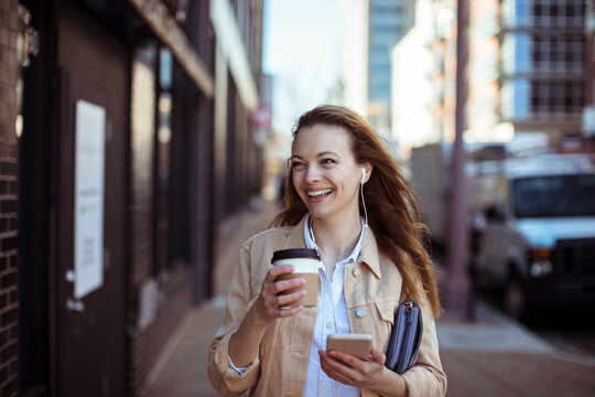 Smiling woman walking in city with coffee and smartphone
