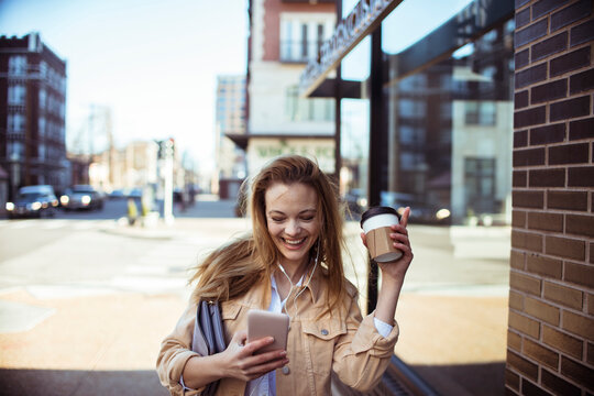Smiling young woman texting with coffee on city street