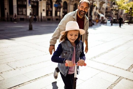 Girl riding kick scooter with father on sunny city street