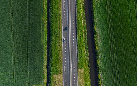 Aerial view of a straight highway with cars driving between lush green agricultural fields and narrow canals Vierpolders, South Holland, Netherlands.
