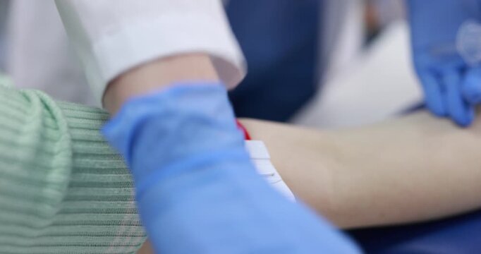 Doctor in protective gloves disinfecting patient's arm and drawing blood sample at white desk, closeup