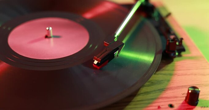 Modern turntable with vinyl record on table in color lights, closeup