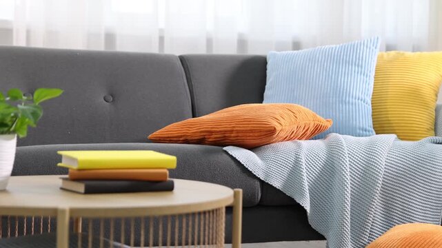 Soft cushions in colorful pillowcases on sofa and table with books indoors. Camera moving right