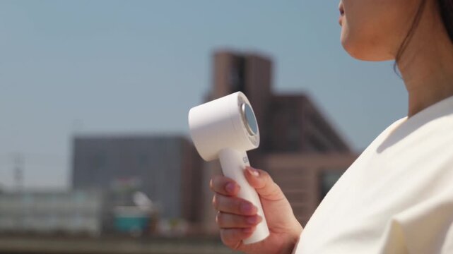 屋外でハンディ扇風機を使う女性 | 夏の暑さ対策・熱中症予防