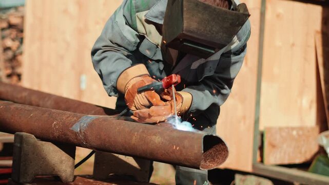 Bright electric welding process on large steel pipe outdoors with intense light and smoke. Skilled industrial worker performs professional metal joining for construction project. Industrial job