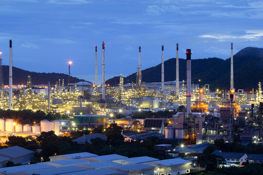 Aerial twilight view of oil refinery complex in Laem Chabang Industrial Estate featuring storage tanks, towering smoke stacks,  industrial infrastructure beneath sky, symbolizes petroleum production.