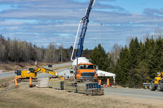 Quebec, Canada, 24 April 2026 : A concrete pump truck and a yellow excavator operate on a roadside construction site next to a highway
