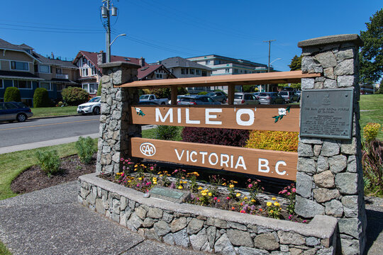 Victoria, BC, CANADA - Jul 1 2024 : The landmark Mile 0 sign marking the western terminus of the Trans-Canada Highway, flanked by stone pillars and a colorful flower garden on a sunny day.