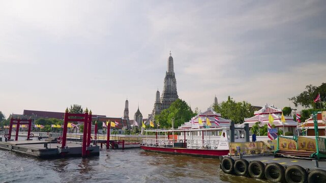 Riverside View Of Wat Arun Temple In Bangkok, Thailand, With Ferry Pier In Foreground. wide pullback shot