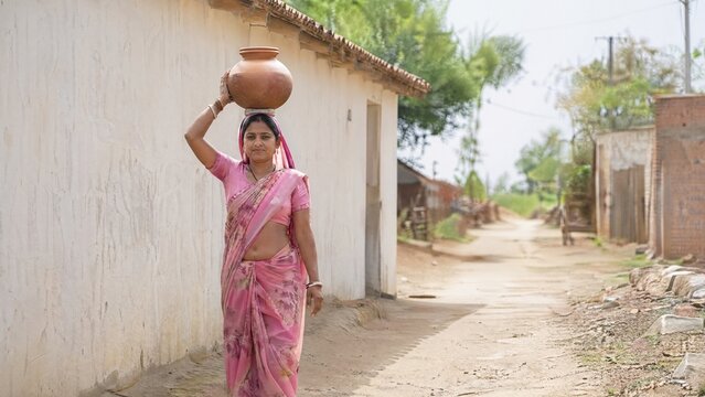 Indian woman walking on dirt road carrying pot on her head  