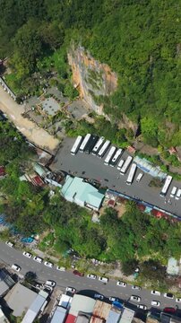 Vertical screen, Vietnam, Da Nang Aerial Bus Depot Near Da Nang Cliff, Parked Coaches And Shuttle Buses, Winding Coastal Road, Dense Green Foothill Vegetation, Tourist Transport Hub, Calm