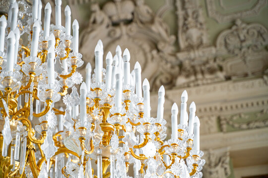  Ornate golden candelabra with tall white candles against carved plaster ceiling in opulent classical baroque interior, luxury heritage concept.