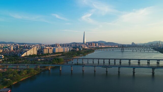 Daytime aerial view captures Seoul cityscape at spring sunset with Lotte World Tower rising above Han River bridges, lush Gwangnaru Hangang Park and blue sky South Korea