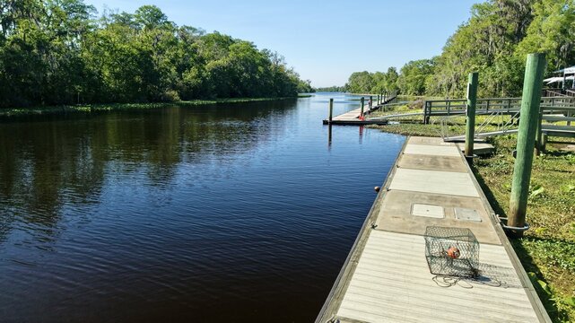 Aerial view of Sixmile Creek with wooden docks, lush green trees, and a crab trap on the pier in St. Johns County, Florida, United States.
