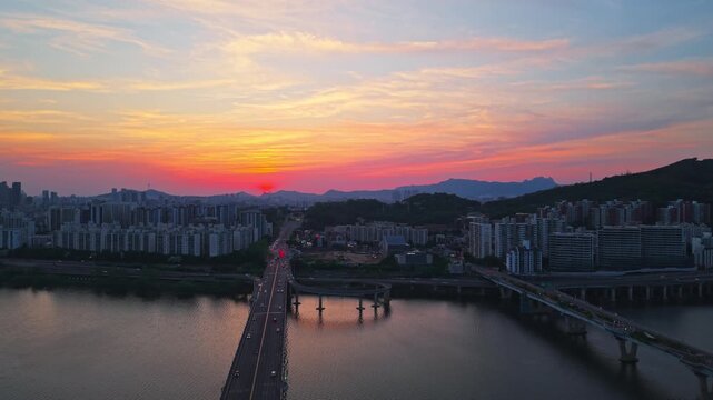 Aerial forward flight over Gwangjin Bridge with evening traffic toward dramatic fiery red sunset sky over Han River with Cheonho Bridge in Seoul