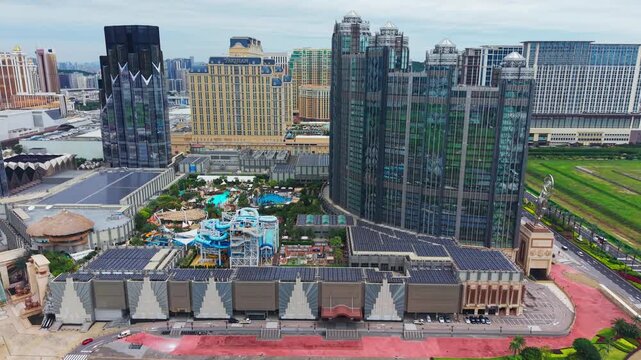 Aerial view of Studio City Macau reveals rooftop solar panels, water park with blue slides and pools, sustainable resort complex on Cotai Strip