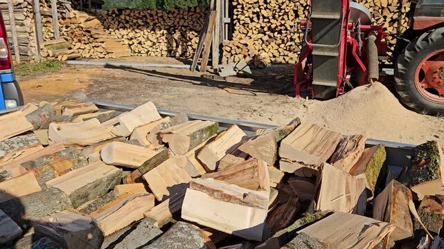 Firewood processing yard with log splitter machine and stacked timber, forestry industry, wood production and rural work.
