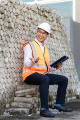 Fototapeta premium A person is standing on a street in a residential area, wearing a white helmet and a bright orange reflective vest, holding a tablet. He is a construction site inspector.