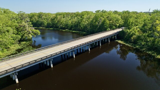 Aerial view of Sixmile Creek bridge crossing dark river water surrounded by dense green forest and lush vegetation in St. Johns County, Florida, United States.
