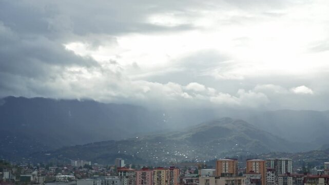Timelapse moving thunderclouds before storm, view of the city near mountains. Sunrays break through the clouds. Stormy weather, melancholy, depression