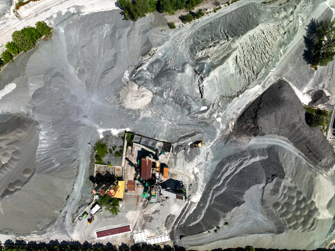 Aerial view of an industrial quarry with large piles of grey gravel and processing machinery in Caprie, Piedmont, Italy.