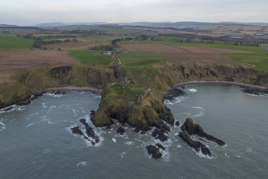 Aerial view of Dunnottar Castle ruins on a dramatic rocky cliff overlooking the sea with green fields in the background Stonehaven, Scotland, United Kingdom.