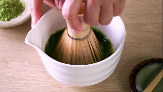 Matcha green tea powder mixing with water in tea bowl by using chasen