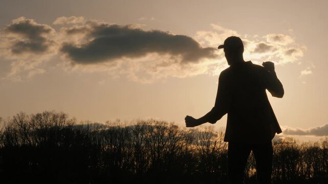 Silhouette of man practicing tai chi at sunset, performing slow and controlled movements, cinematic dynamic footage.