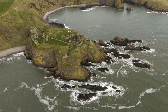 Aerial view of the medieval ruins of Dunnottar Castle perched on a rocky headland surrounded by the North Sea and green coastal cliffs in Stonehaven, Scotland, United Kingdom.