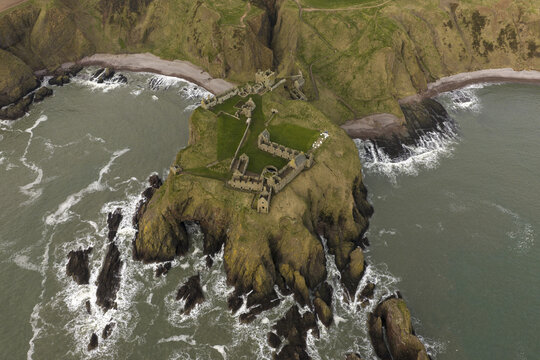 Aerial view of Dunnottar Castle situated on a dramatic rocky headland surrounded by the North Sea and green cliffs in Stonehaven, Scotland, United Kingdom.