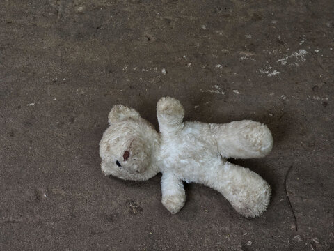 Abandoned dirty teddy bear plush toy lying on cold ground conveying sad lonely feeling of lost childhood and forgotten memories left behind alone