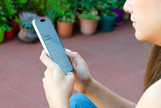 Mujer escribiendo chat de IA en aplicaci&oacute;n m&oacute;vil de su tel&eacute;fono, sentada en el patio de casa. vista de perfil.