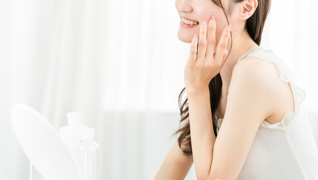 Asian woman in the mirror doing skincare (moisturizing, beauty, cosmetics, skin, anti-aging)