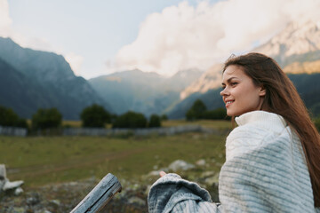 Obraz premium Woman sits outdoors in a cozy sweater overlooking mountain scenery, enjoying a peaceful lifestyle moment in nature, casual and serene in the countryside