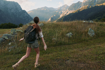 Naklejka premium A woman hiking with a backpack across a mountain meadow, exploring rugged landscape under clear skies. A lifestyle moment of outdoor adventure and nature connection.