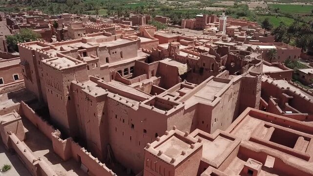 Drone view of a large traditional kasbah complex in Ouarzazate, Morocco, highlighting courtyards, adobe walls, and architectural layout surrounded by oasis vegetation. Ideal for cultural, architectura