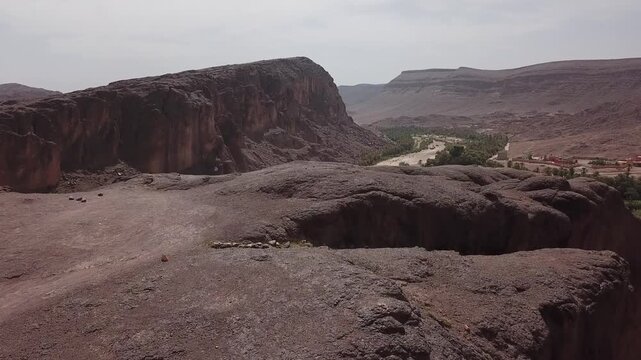 Aerial drone footage of a dramatic desert canyon with towering cliffs and a winding river flowing through an oasis valley in Ouarzazate, Morocco. Strong depth and natural composition ideal for cinemat