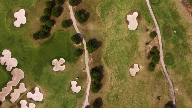 Top-down view of a golf course featuring sand bunkers, fairways, cart paths and scattered trees across manicured green grass