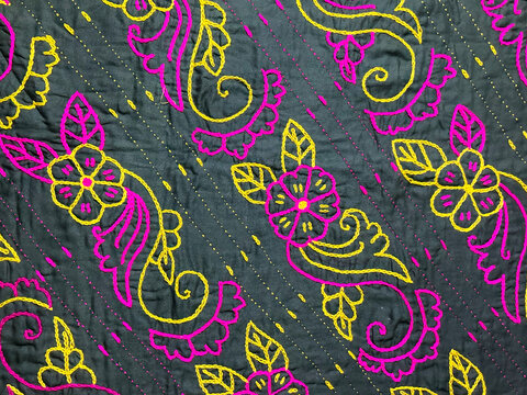 Dark grey cotton fabric featuring handmade pink and yellow floral kantha embroidery, traditional Indian needlework texture for ethnic fashion backdrop, macro photography