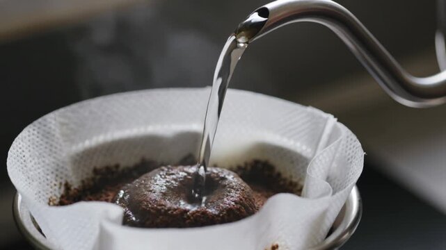 Hot water pouring from kettle into coffee grounds for pour over brew. Close-up macro of barista making fresh coffee in kitchen.