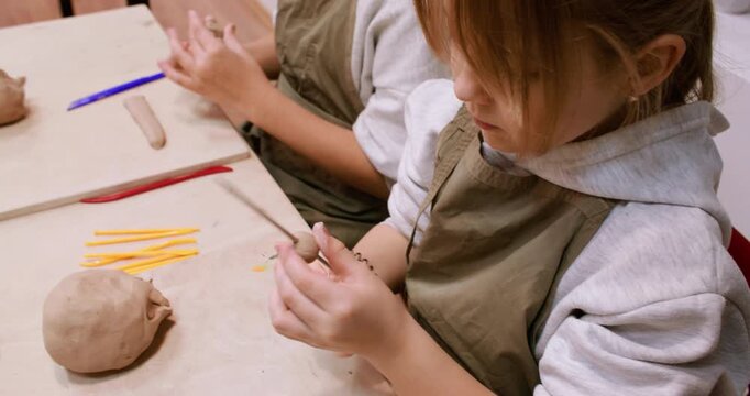 Children pottery. Artisan master class. Two creative kids shaping ceramic molding raw clay using color tool in professional art studio.