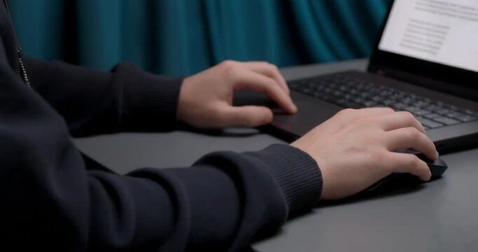 Person working on laptop computer while using wireless mouse at desk close up shot.